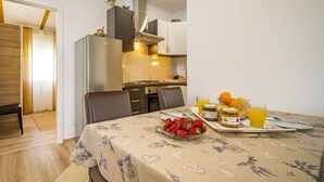 Un coin repas avec une table dressée pour deux personnes, agrémentée d’une nappe à motifs floraux, d’un bol de fraises et d’un plateau contenant des pots de confiture et un verre de jus d’orange.