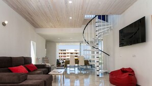 Ein modernes Wohnzimmer mit einem braunen Sofa, einem roten Sitzsack, einer weißen Wendeltreppe und einem flachbildfernseher an der Wand.