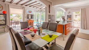 Una cocina moderna con una isla central, comedor con sillas y vista a una piscina.