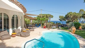 Una piscina con zona de sillones de descanso, un porche cubierto y vista al mar.