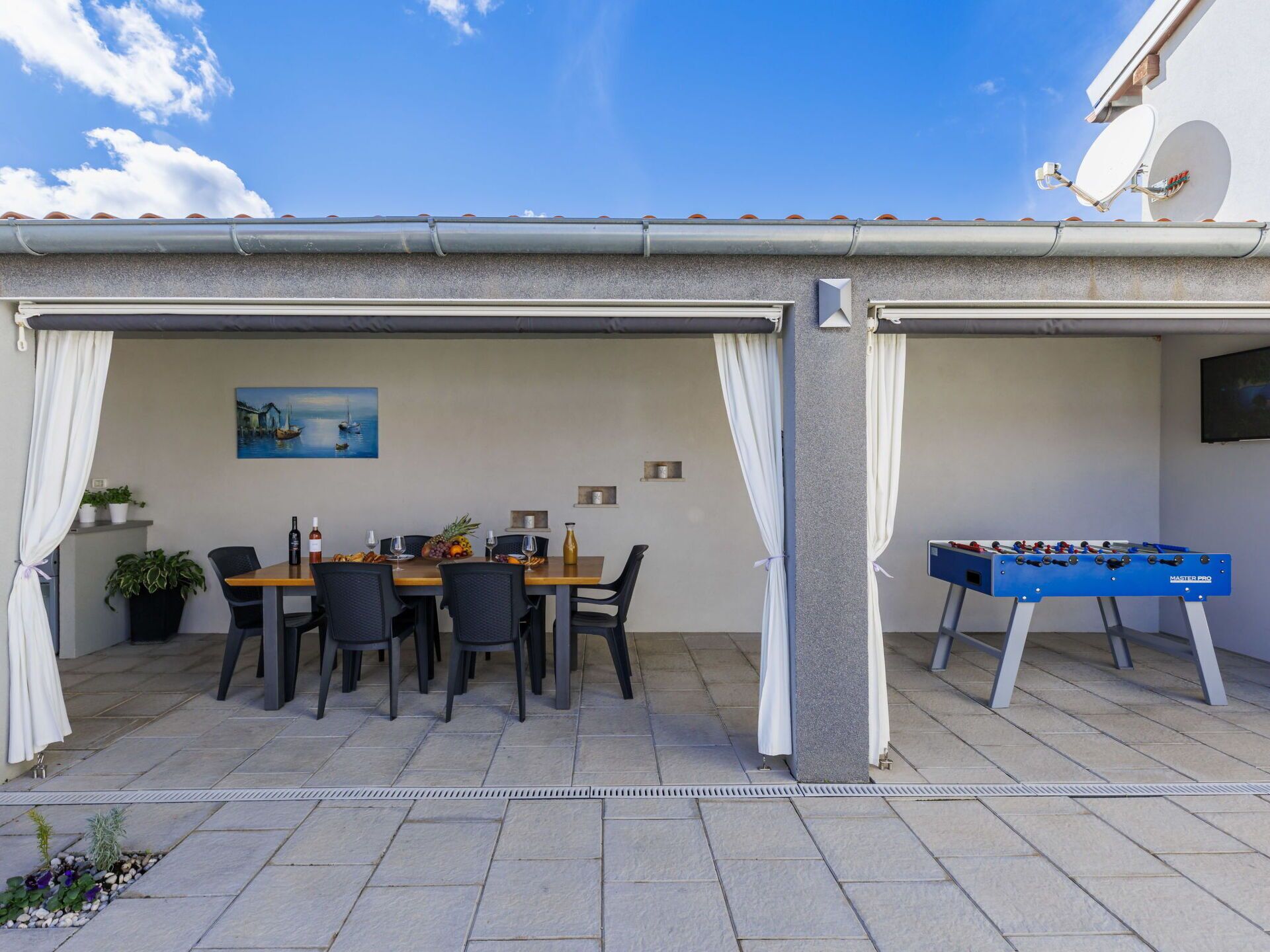 Un patio al aire libre con una mesa de comedor, sillas, una mesa de fútbol de mesa y un cuadro en la pared.
