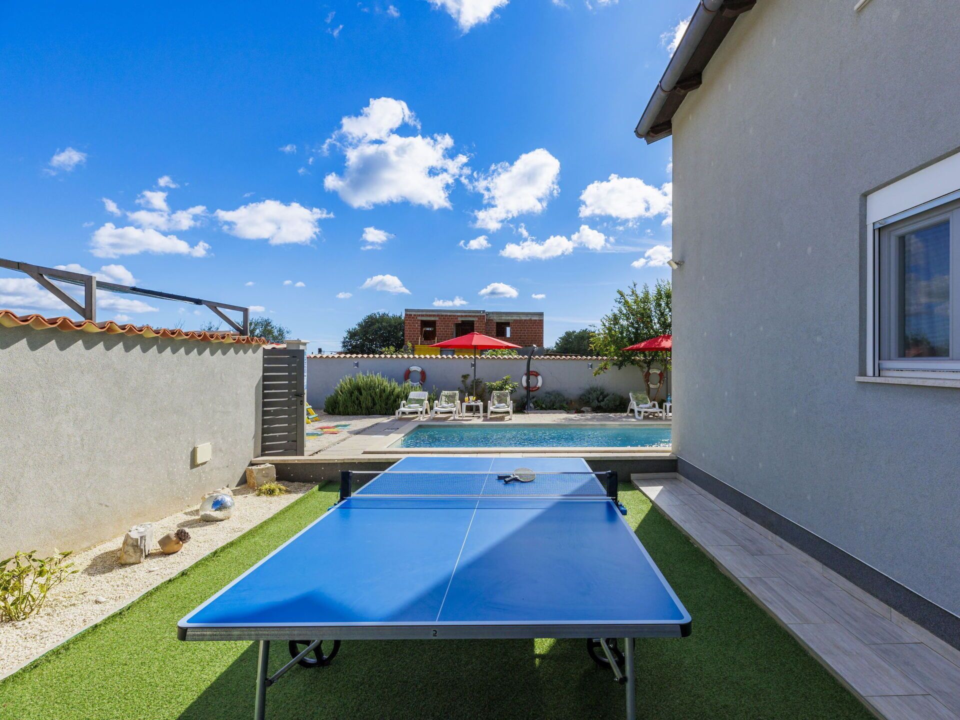 Een pooltafel in een achtertuin met een helderblauwe lucht en een gebouw op de achtergrond.