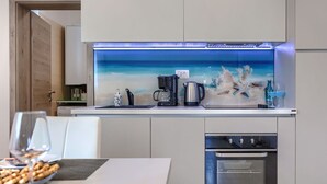 A modern kitchen with a built-in island, a coffee maker, a kettle, and a view of the ocean through a window.