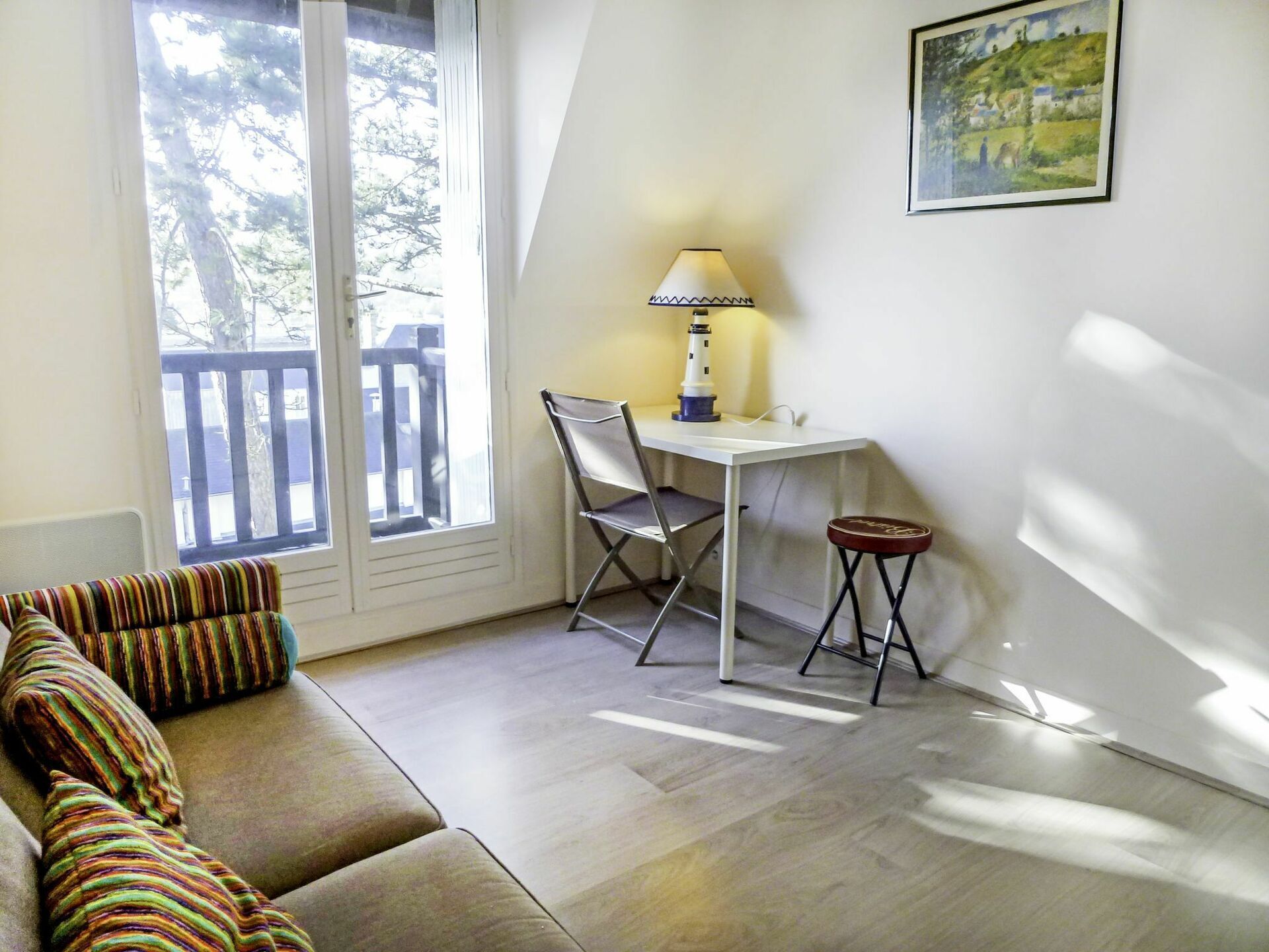 Une pièce comprenant un canapé, un bureau, une chaise, un petit tabouret et un tableau accroché au mur.