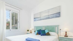 Een slaapkamer met een bed, nachtkastje, lamp, raam en een schilderij aan de muur.