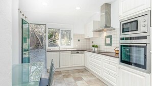 Een moderne keuken met witte kastjes, een glazen eettafel en twee ovens.