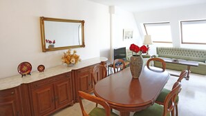 A dining area with a wooden table and chairs, a vase with red flowers, a mirror, and a green sofa in the background. - Cosy apartment for 6 guests with WIFI, A/C, TV, terrace and pets allowed (L'ampolla)