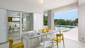 Un espace repas moderne avec une table et des chaises, une cuisine en arrière-plan et une vue sur la piscine.