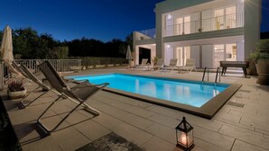 Une maison moderne à deux étages, dotée d’une piscine, d’un espace salon extérieur et d’un balcon bien éclairé.