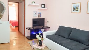 Ein Wohnzimmer mit einer Couch, einem Glastisch mit einer Vase, einem Fernseher auf einem Schrank und einer Tür zu einem anderen Raum.