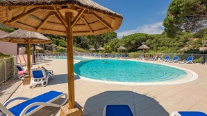 Un área de piscina con sillas reclinables azules, sombrillas de paja y una piscina azul cristalina.
