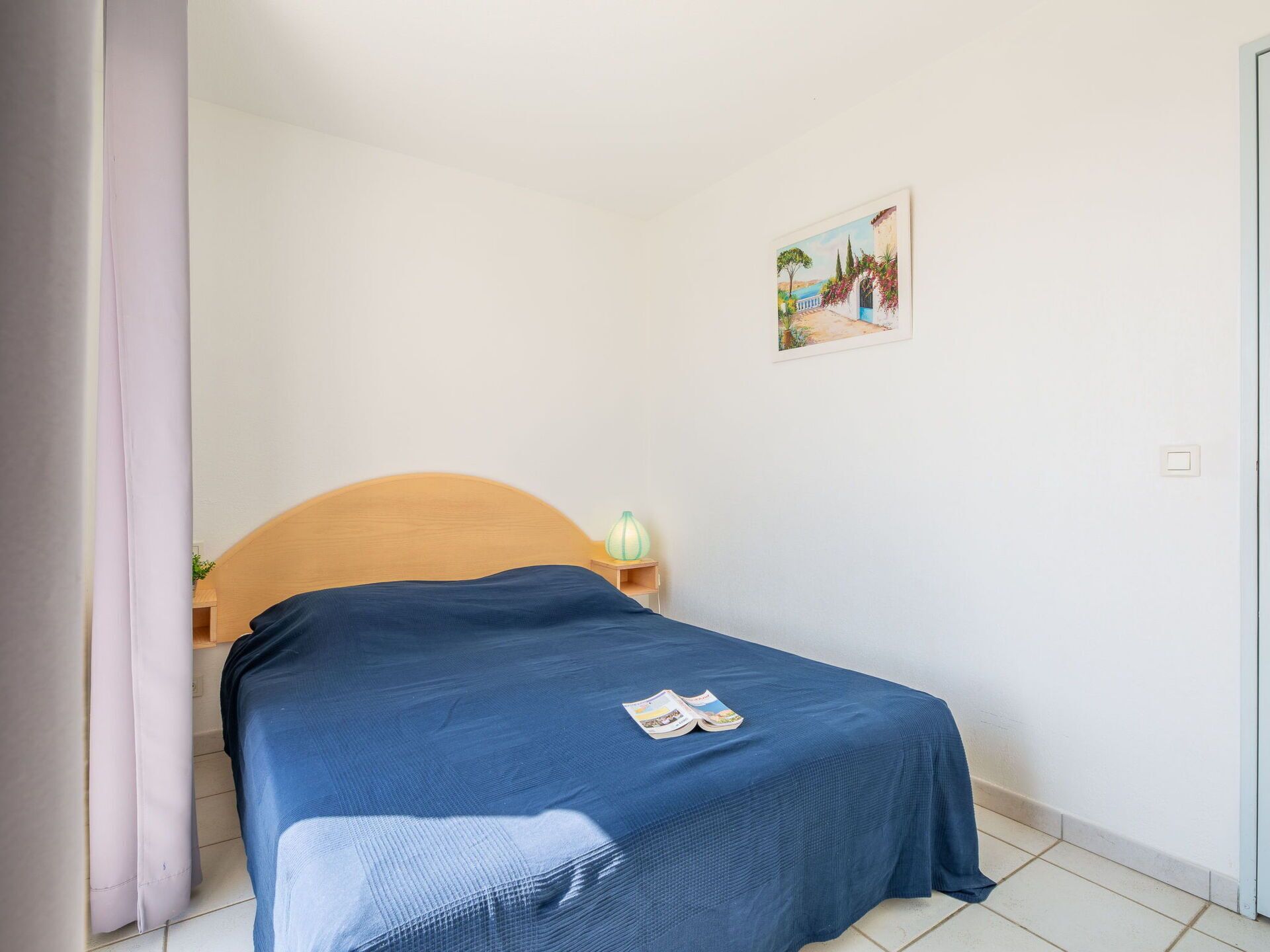 A single bed with a wooden headboard, a nightstand with a lamp, and a framed picture on the wall.