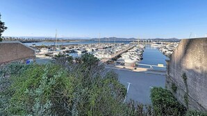 Un puerto deportivo con barcos amarrados, cielo despejado y montañas a lo lejos.