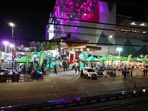 A nighttime urban scene with a brightly lit building and green tents. - Hybrit Hostel & Cafe (Hat Yai)