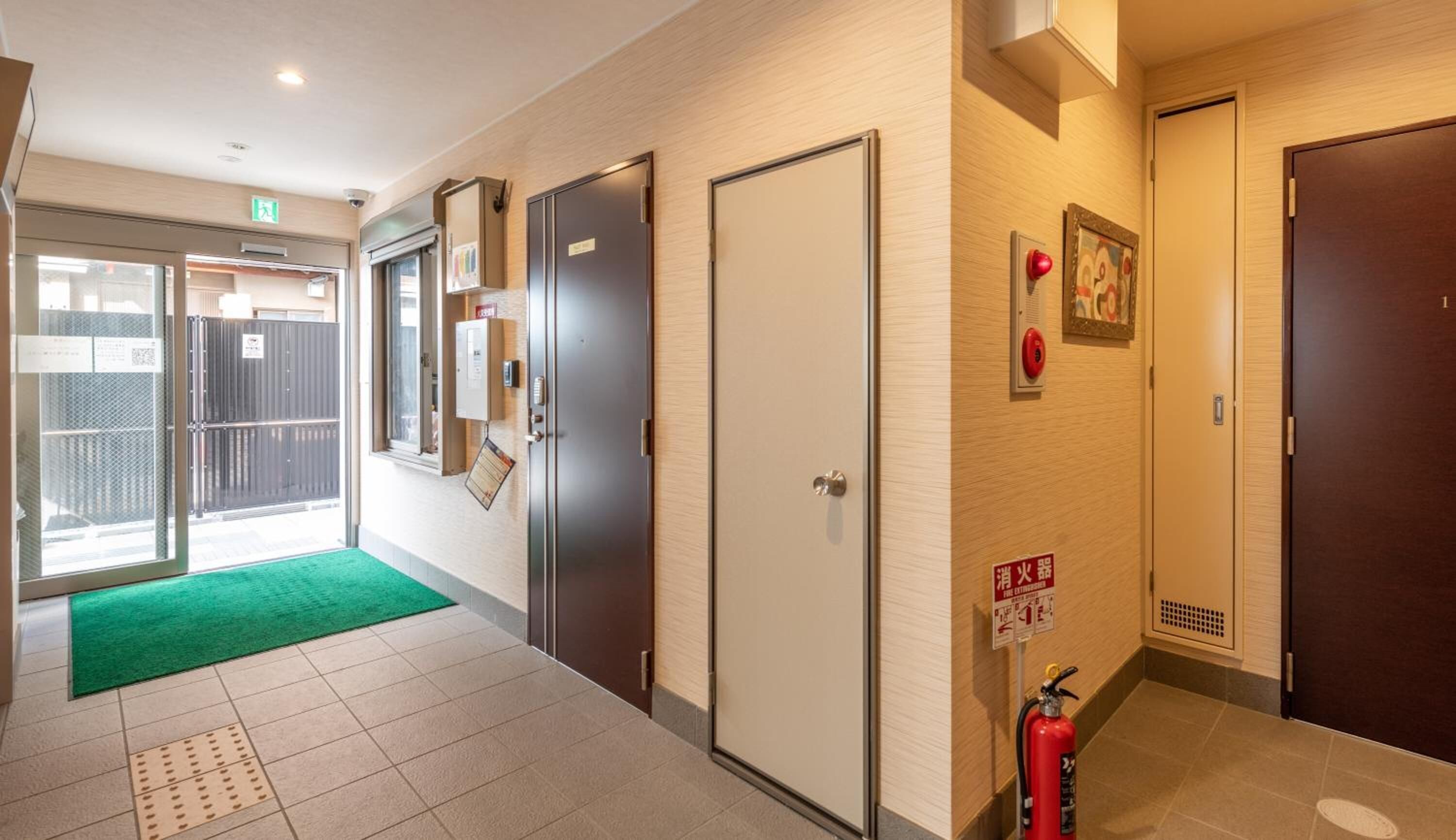 A hallway with a green carpet, a fire extinguisher, and a door with a fire alarm sign.
