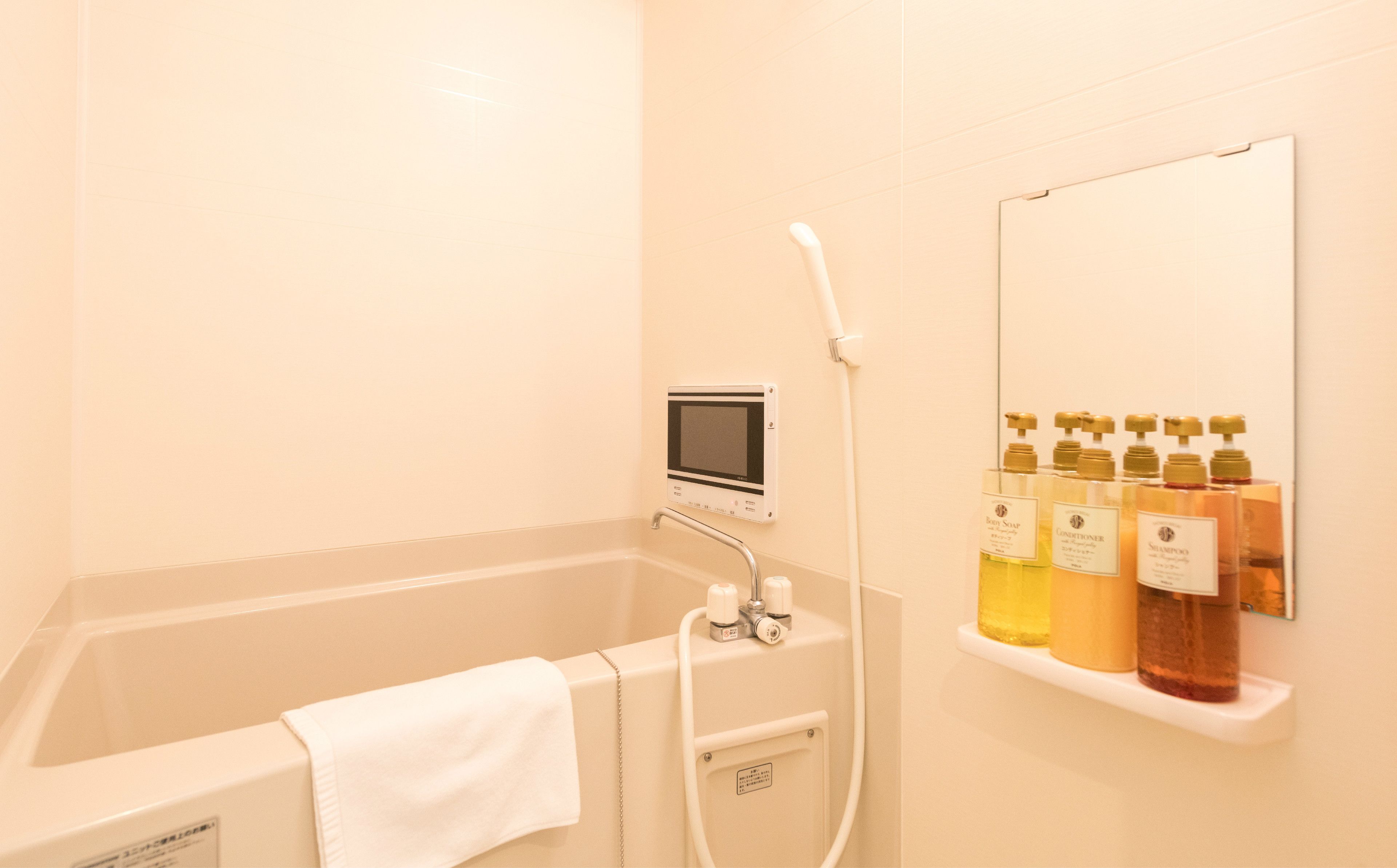 Casa de banho com banheira, chuveiro manual, painel de controlo digital e prateleira com produtos de higiene pessoal.