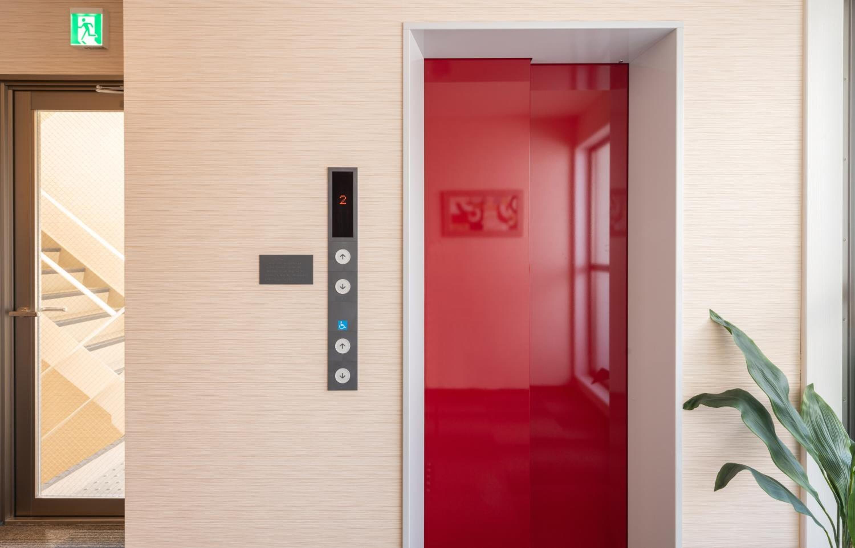 An elevator with a digital display and buttons, a staircase, and a plant.