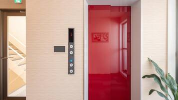An elevator with a digital display and buttons, a staircase, and a plant.