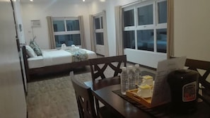 A hotel room with a bed, a desk with a chair, a window, and a table with a bottle and a menu. - Bikyeong Hotel and Restaurant (Tagaytay)