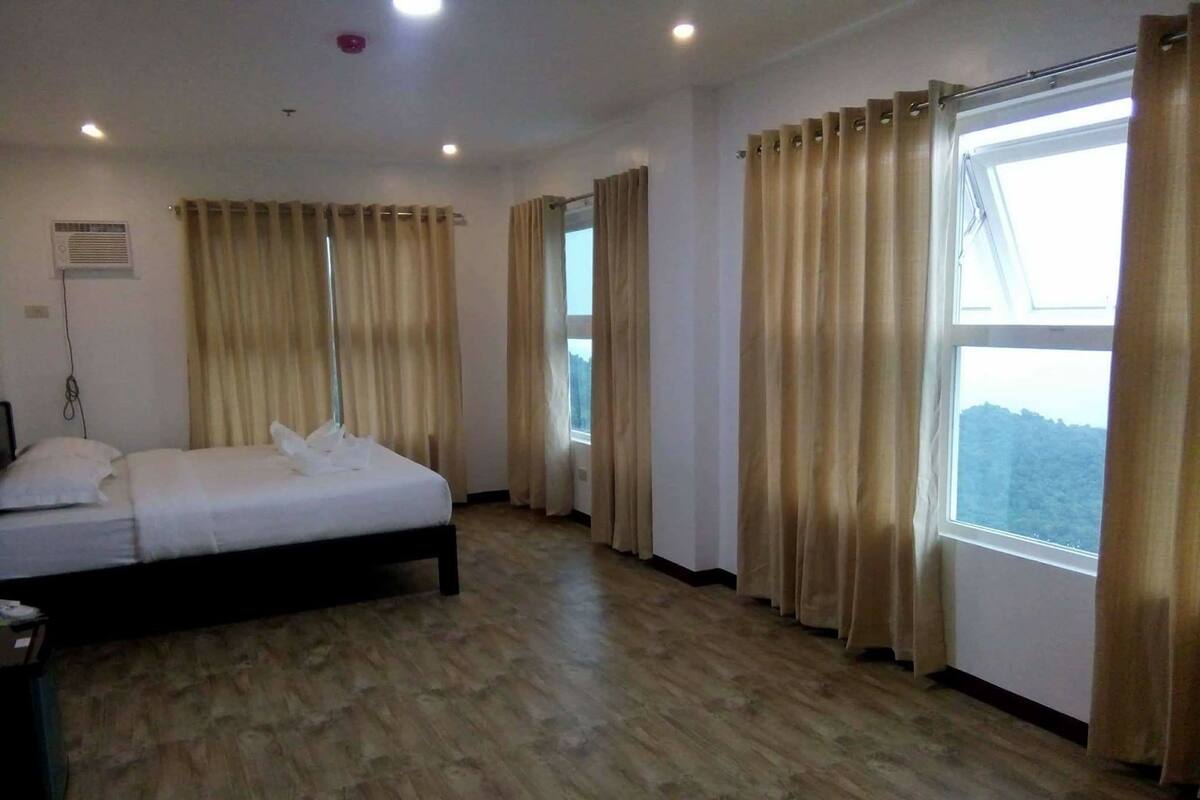 A hotel room with a bed, curtains, a window, and a wooden floor.