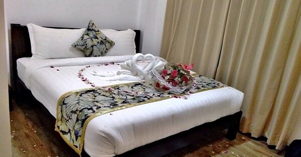 A neatly made bed with a floral bedspread, a heart-shaped towel arrangement, and a bouquet of flowers. - Bikyeong Hotel and Restaurant (Tagaytay)