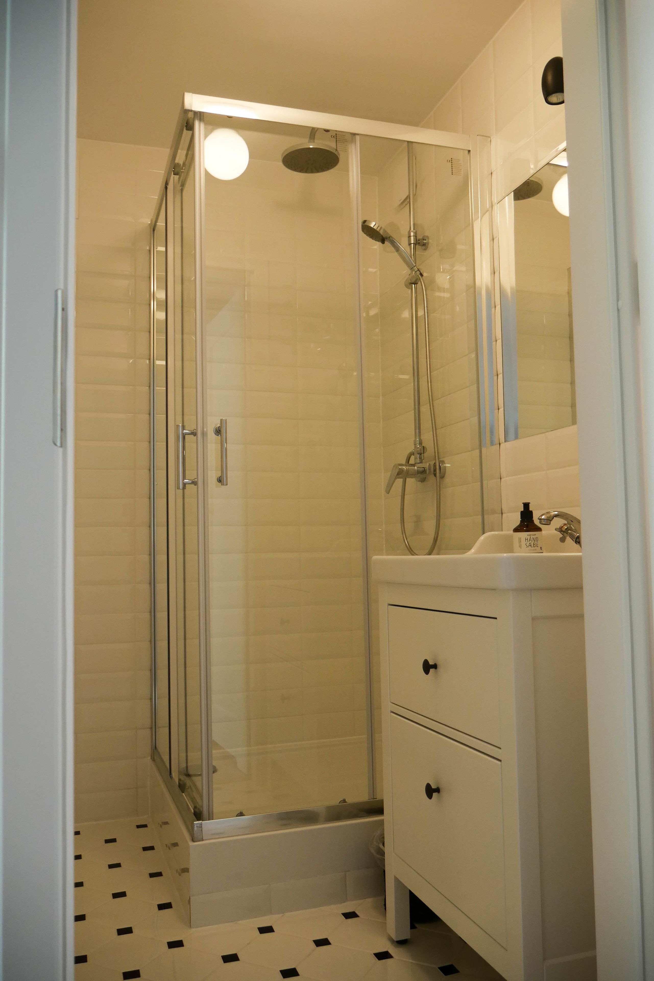 A bathroom with a glass-enclosed shower, a white sink with a mirror above it, and a tiled floor.