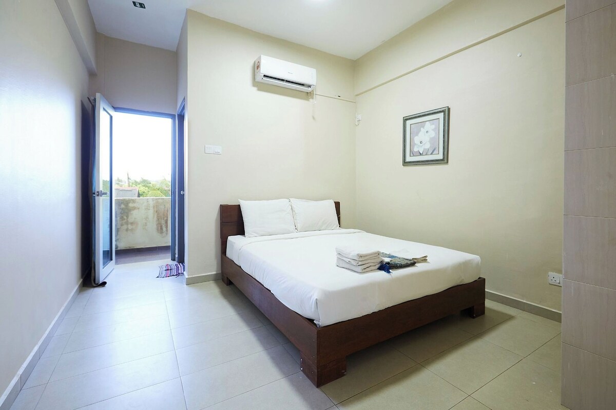 A bedroom with a bed, an air conditioning unit, a framed picture, and a view through an open door.