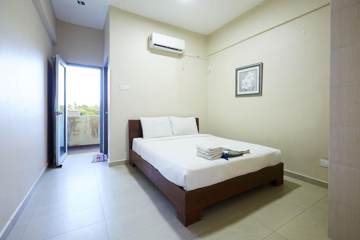 A bedroom with a bed, an air conditioning unit, a framed picture, and a view through an open door.