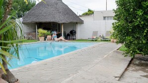 Ein Schwimmbecken mit einer strohgedeckten Struktur, Blumentöpfen und einem gepflasterten Weg.