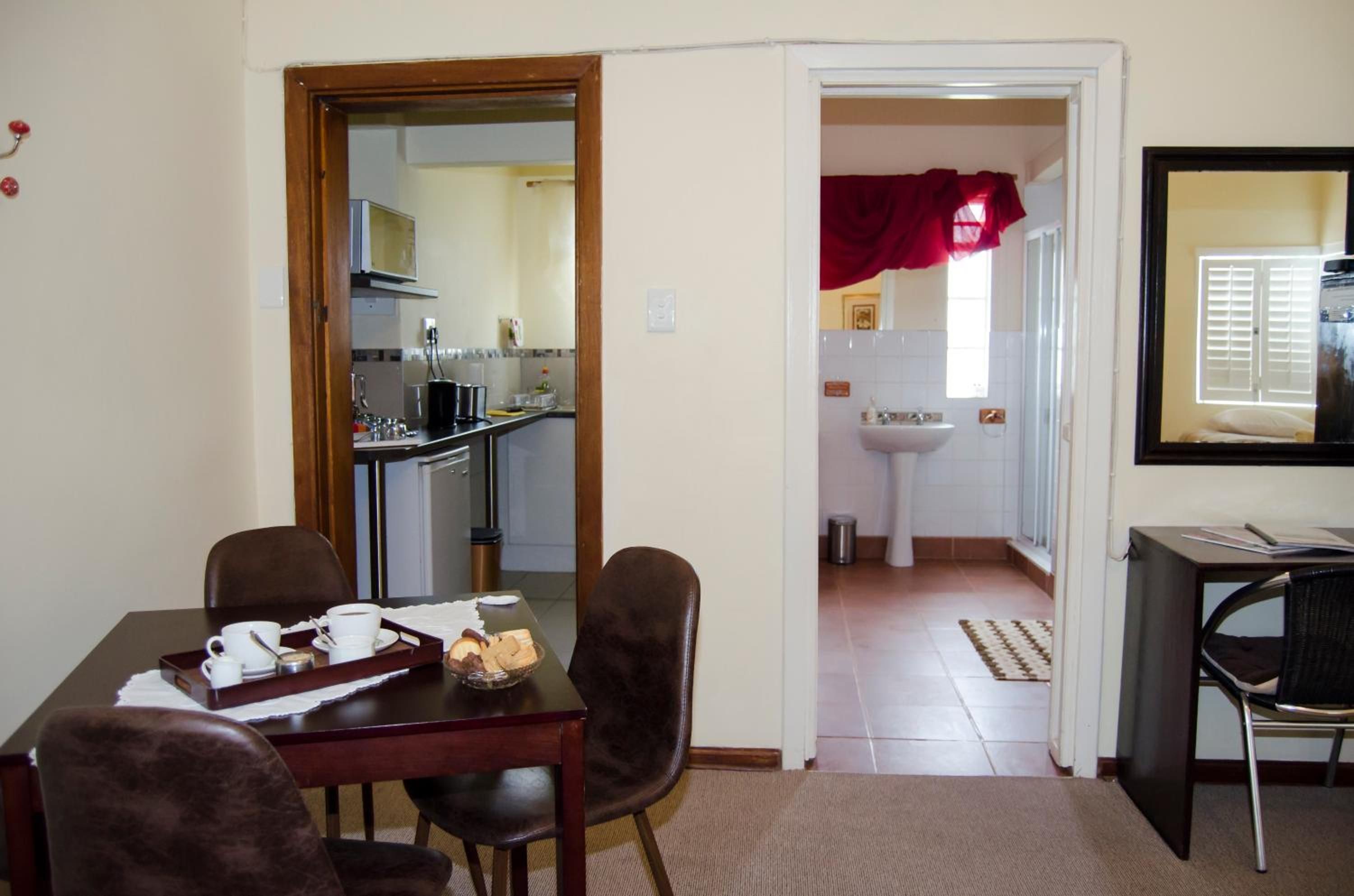 A dining area with a table set for two, a kitchen in the background, and a bathroom visible through an open door.
