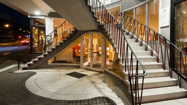 Une entrée d’hôtel moderne, avec un escalier en colimaçon, des portes vitrées et un intérieur bien éclairé.