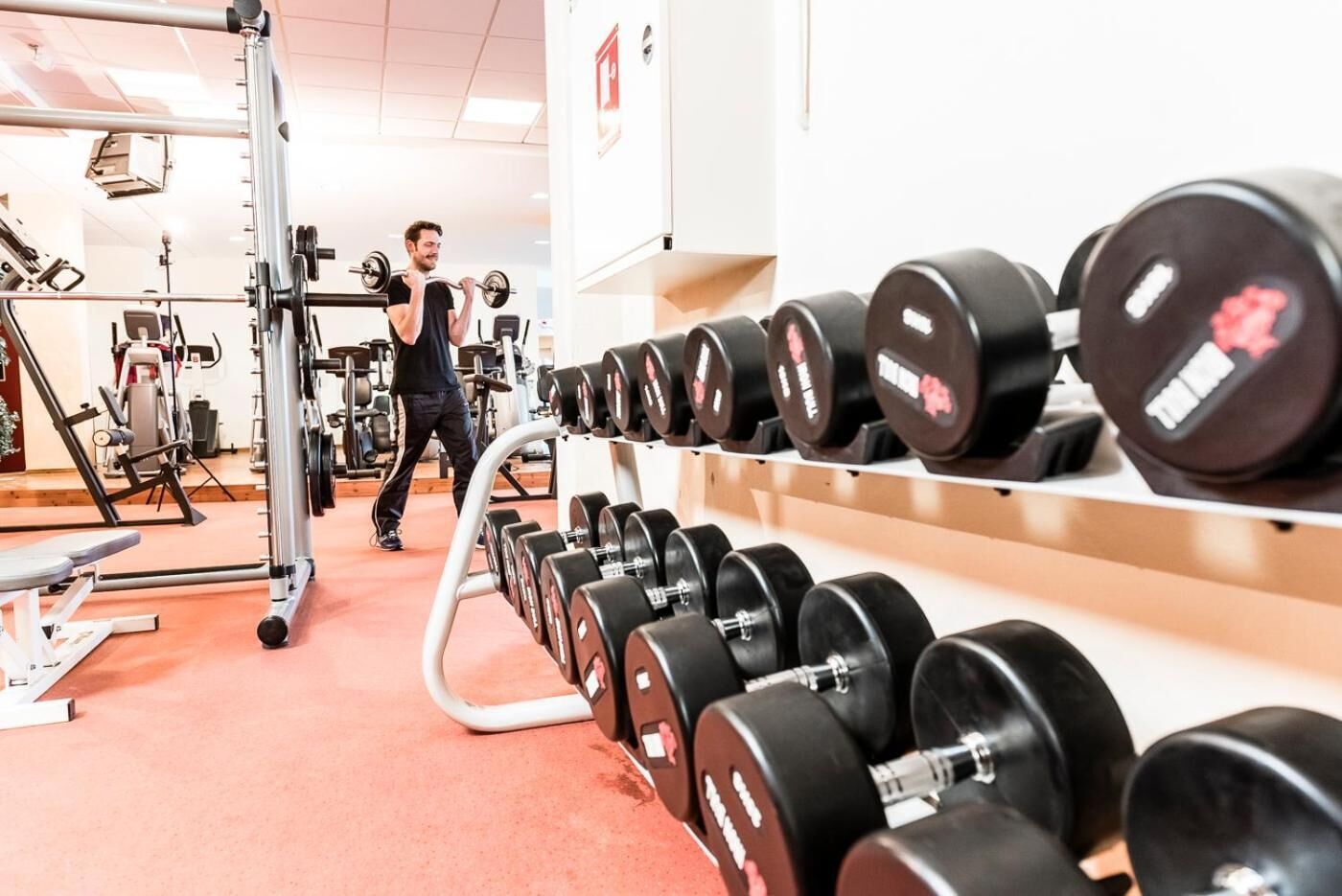 Un gimnasio con equipo de levantamiento de pesas y mancuernas.