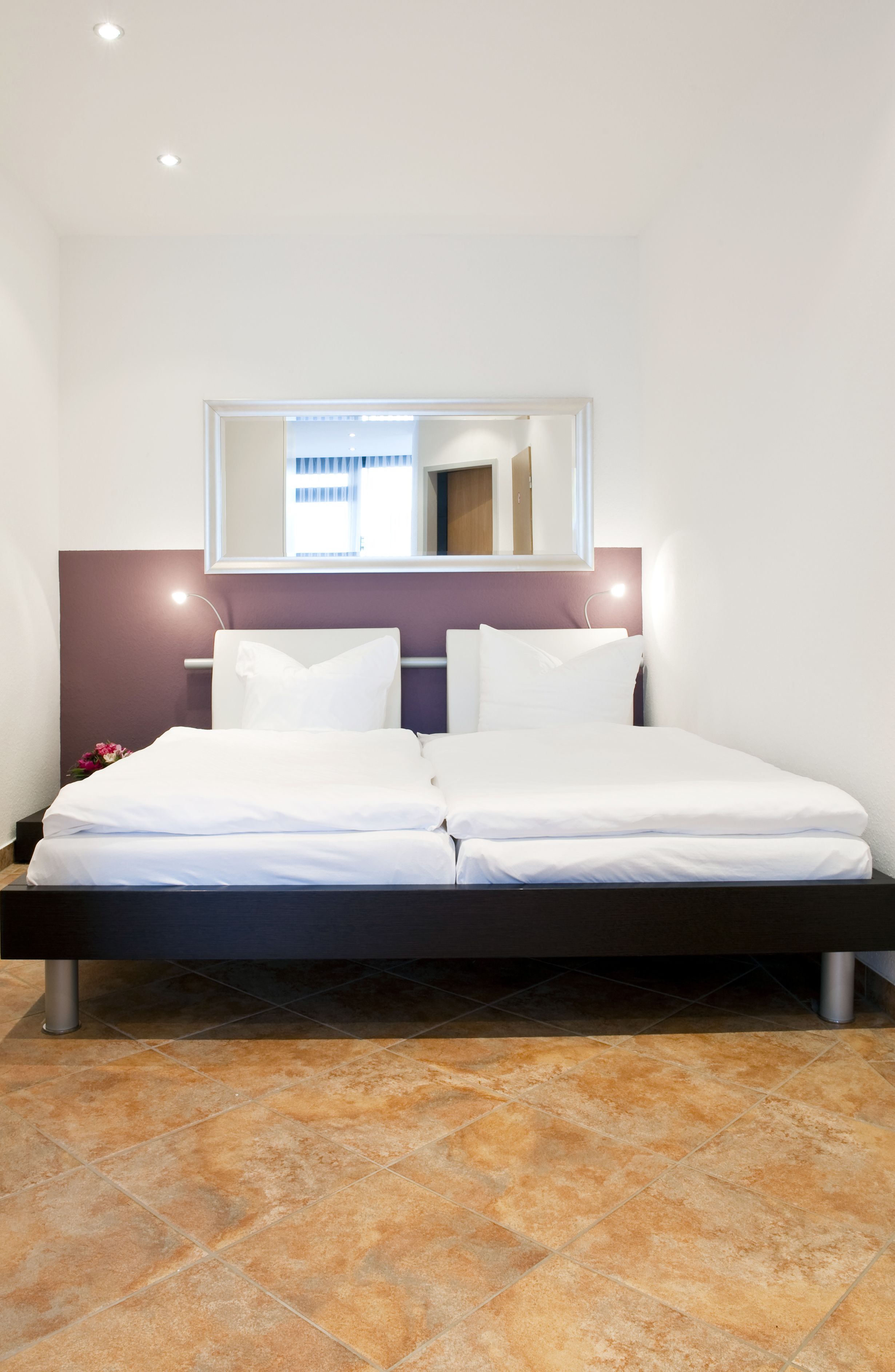 A neatly made bed with white linens, a headboard with a mirror, and a bedside lamp.