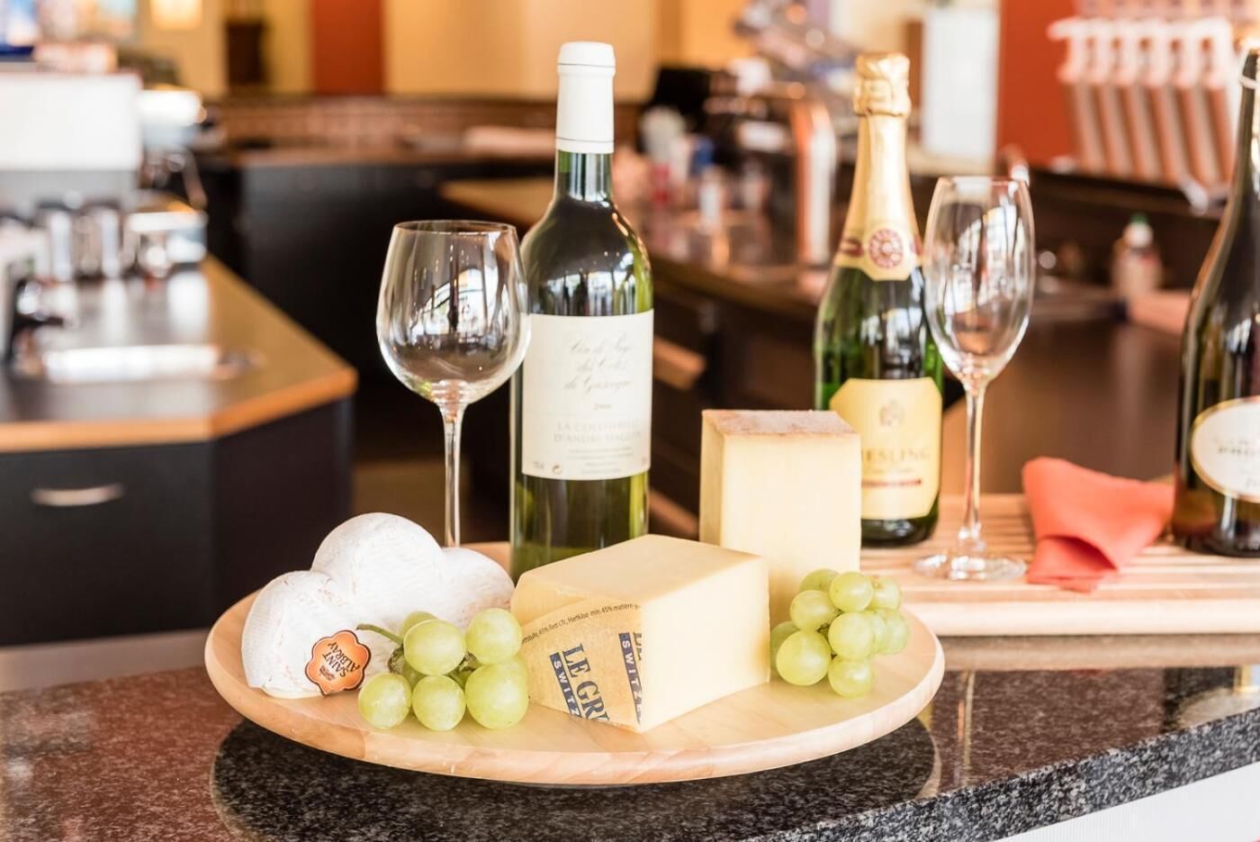 Une planche à fromages avec divers fromages, des raisins et des bouteilles de vin, le tout posé sur un comptoir.