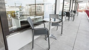 Un espace extérieur moderne, aménagé avec des fauteuils en osier et une table en verre, offrant une vue sur le paysage urbain.