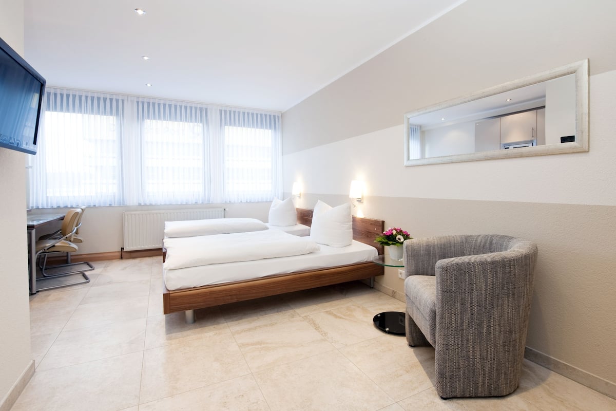 A modern hotel room with a bed, a desk, a chair, and a large window with curtains.
