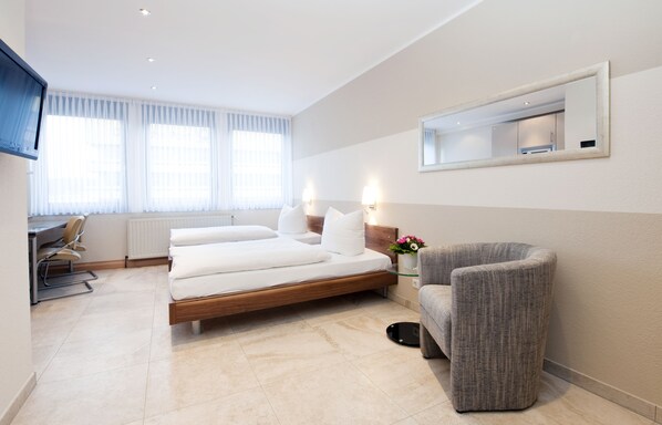 Una habitación de hotel moderna con cama, escritorio, silla y un amplio ventanal con cortinas.