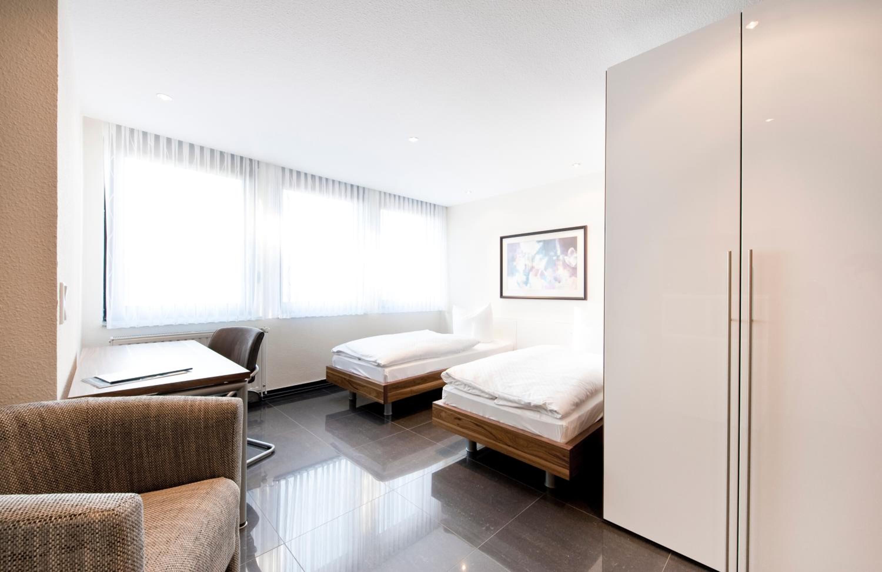 Une chambre d’hôtel avec deux lits, un bureau, une chaise et une armoire.