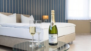 Une chambre d’hôtel avec un lit, une table en verre sur laquelle se trouve une bouteille de Cuvée Laurent et deux verres de vin blanc.