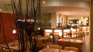 Un restaurant moderne doté d’un bar incurvé, de chaises jaunes et d’un espace de restauration central avec des tables.