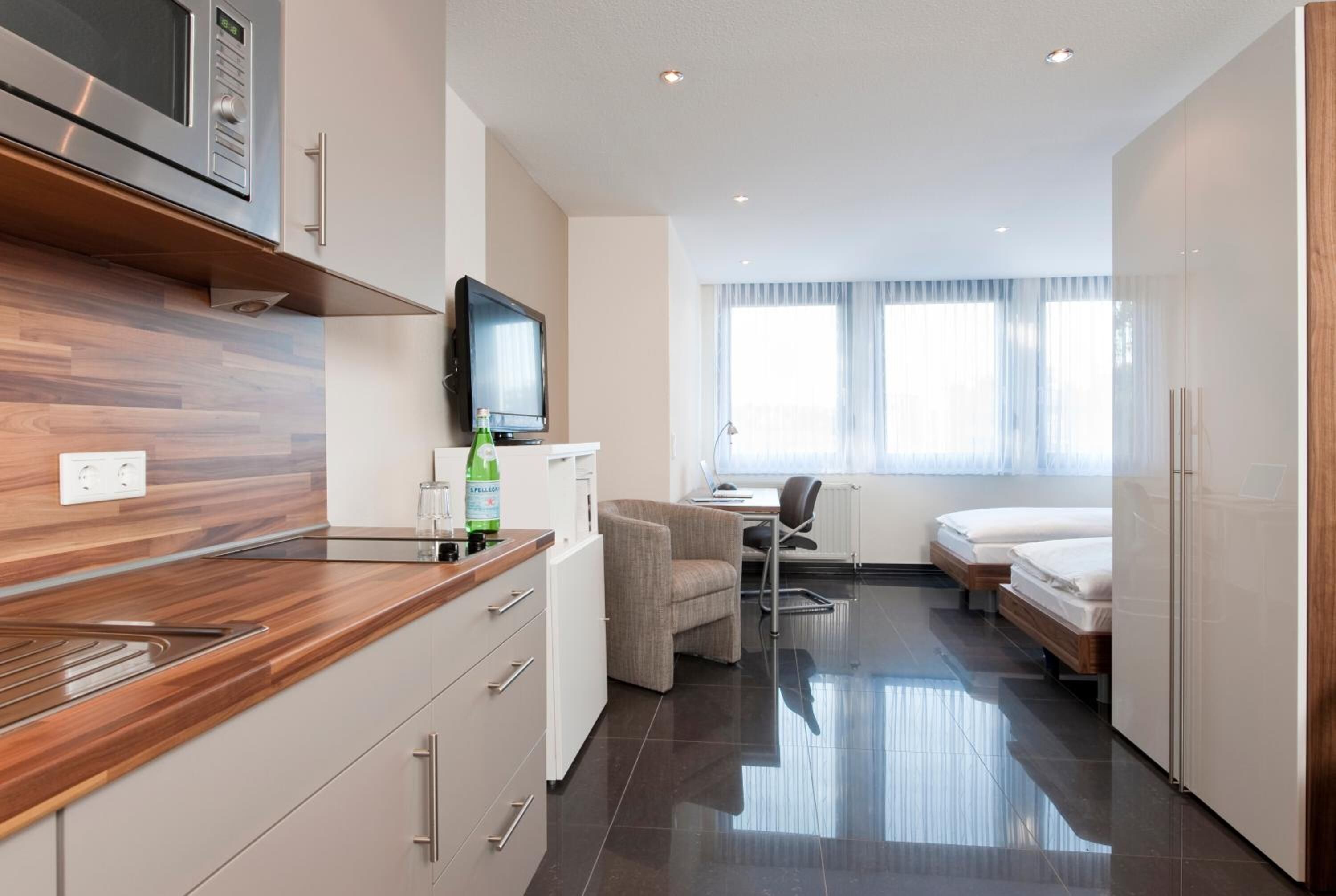 Habitació d'hotel moderna amb cuineta, televisió de pantalla plana, un llit i escriptori.
