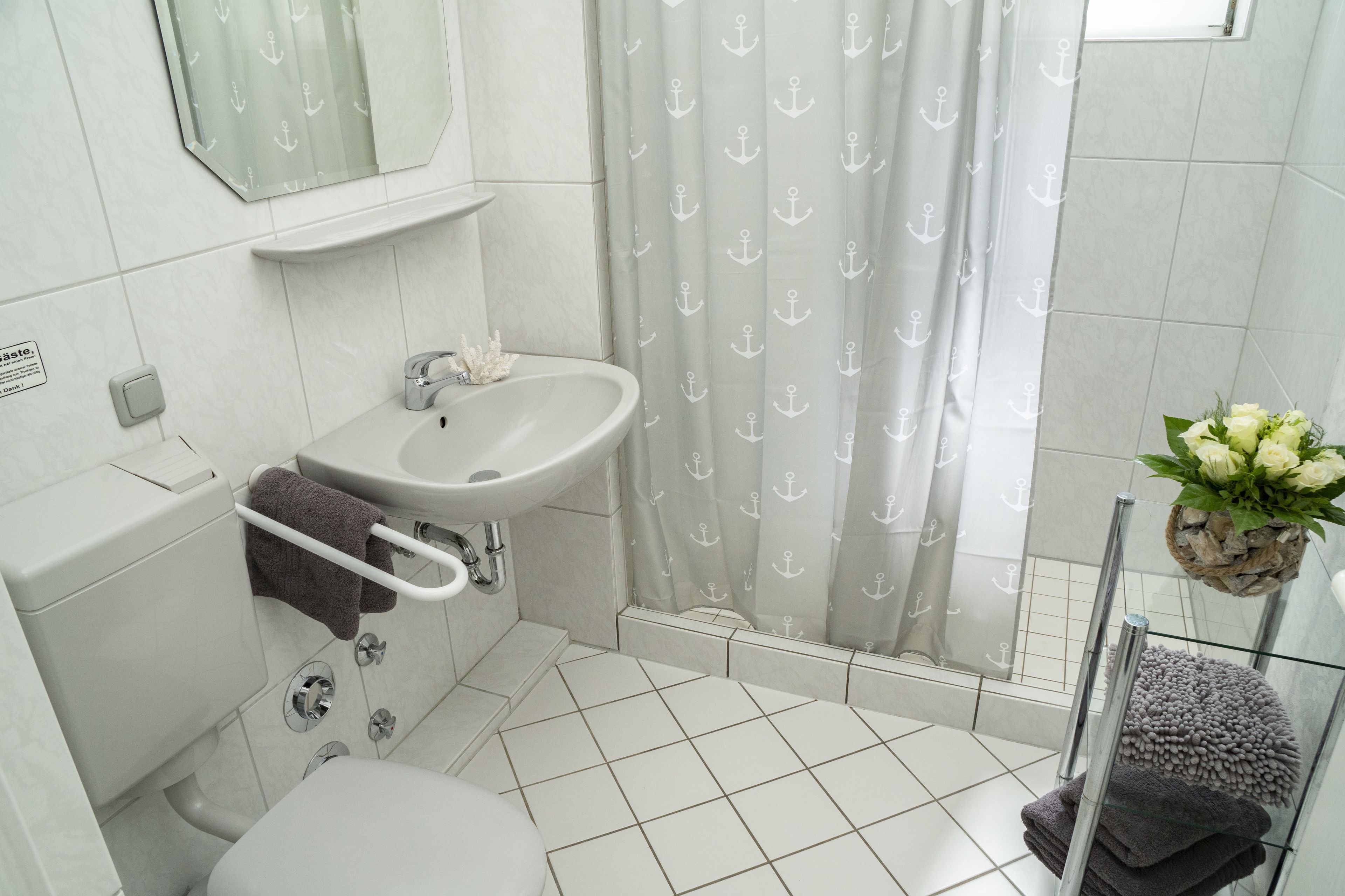 A bathroom with a toilet, sink, and shower curtain with anchor patterns.