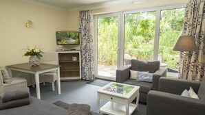 A living room with a sofa, armchair, coffee table, and a TV on a stand. - Apartment-Hotel Dieksee Eck (Malente)