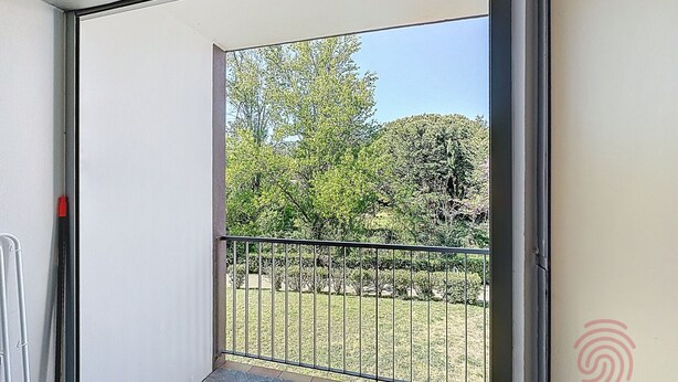 A balcony with a metal railing, a view of trees and grass, and a door with a red handle. - Cozy Apartment with Terrace, Near Spa and Town Center, Pet-Friendly, Free Parking, 24m² (Lamalou-les-Bains)