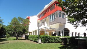 A building with a red and white facade, multiple balconies, and a covered outdoor area with umbrellas. - Cozy Apartment with Terrace, Near Spa and Town Center, Pet-Friendly, Free Parking, 24m² (Lamalou-les-Bains)