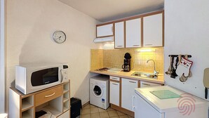 A compact kitchen with a microwave, washing machine, sink, and cabinets. - Cozy Apartment with Terrace, Near Spa and Town Center, Pet-Friendly, Free Parking, 24m² (Lamalou-les-Bains)