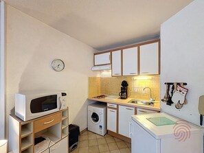 Una cucina compatta con forno a microonde, lavatrice, lavandino e pensili.