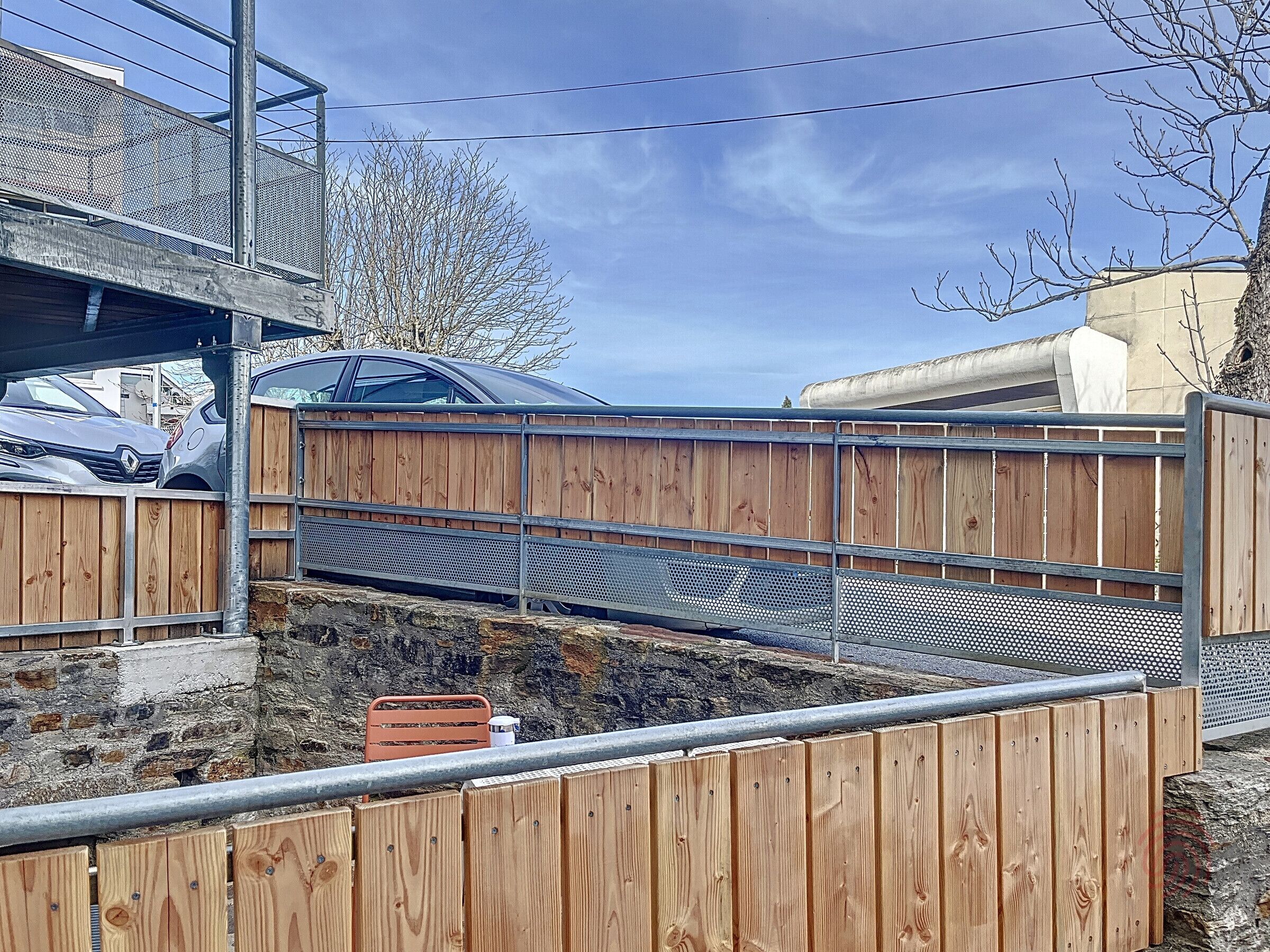 A wooden fence with a metal gate, a parked car, and a stone wall in the background.