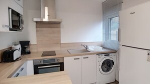 A compact kitchen with a microwave, coffee maker, oven, sink, and washing machine.