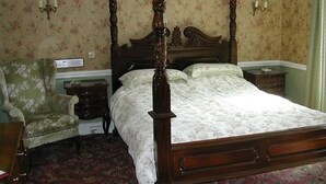 A four-poster bed with a floral-patterned bedspread, a wooden nightstand, a green upholstered armchair, and a floral-patterned carpet. - Neuadd Arms Hotel (Llanwrtyd Wells)